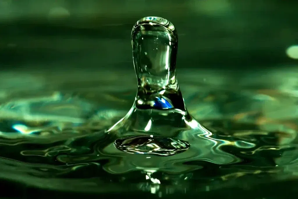 A serene digital painting of a Hindu man in traditional white attire standing by a river at sunrise, performing a water offering (Arghya). A glowing, golden Surya Yantra hologram is suspended in the sky above the water, surrounded by a soft rainbow halo and Sanskrit mantras.