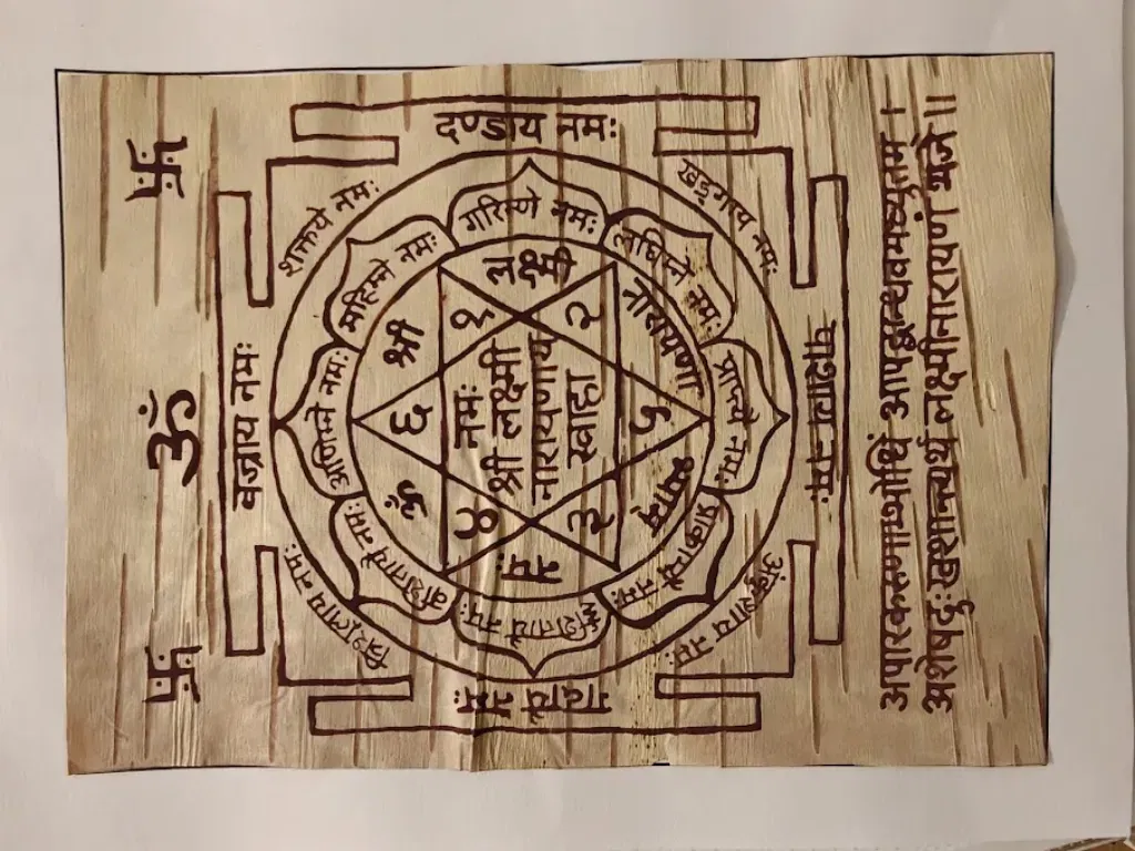 A top-down, detailed view of a completed, hand-drawn Yantra on a rectangular sheet of textured Himalayan Bhojpatra. The central design features a complex star polygon enclosed within concentric circles and a square "Bhupura" border with four ceremonial gates. The Yantra is inscribed with precise Sanskrit calligraphy using traditional maroon Ashtagandha ink, featuring the central mantra "Om Namah Shri Lakshmi Narayanaya Swaha." Sacred symbols like the Om and Swastika are positioned on the left margin, while a vertical Sanskrit verse is inscribed on the right.